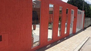 A red building with large windows and a tiled walkway. - Toca Hospedaria (São Bento do Sapucaí)