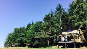 Une cabane dotée d’une terrasse et d’un petit porche, entourée d’une forêt dense.