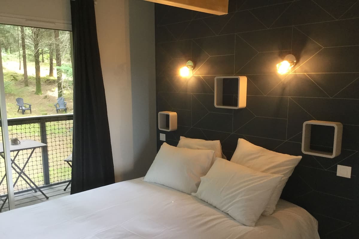 Une chambre à coucher avec un grand lit, deux tables de chevet et une vue sur l’extérieur par une fenêtre.