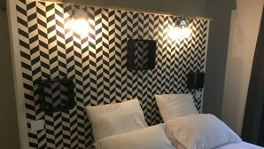 Un lit avec une literie blanche dans une pièce dont un mur est décoré d’un motif en chevrons noir et blanc.