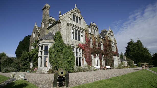 A large, historic stone building with a prominent turret and ivy-covered walls.