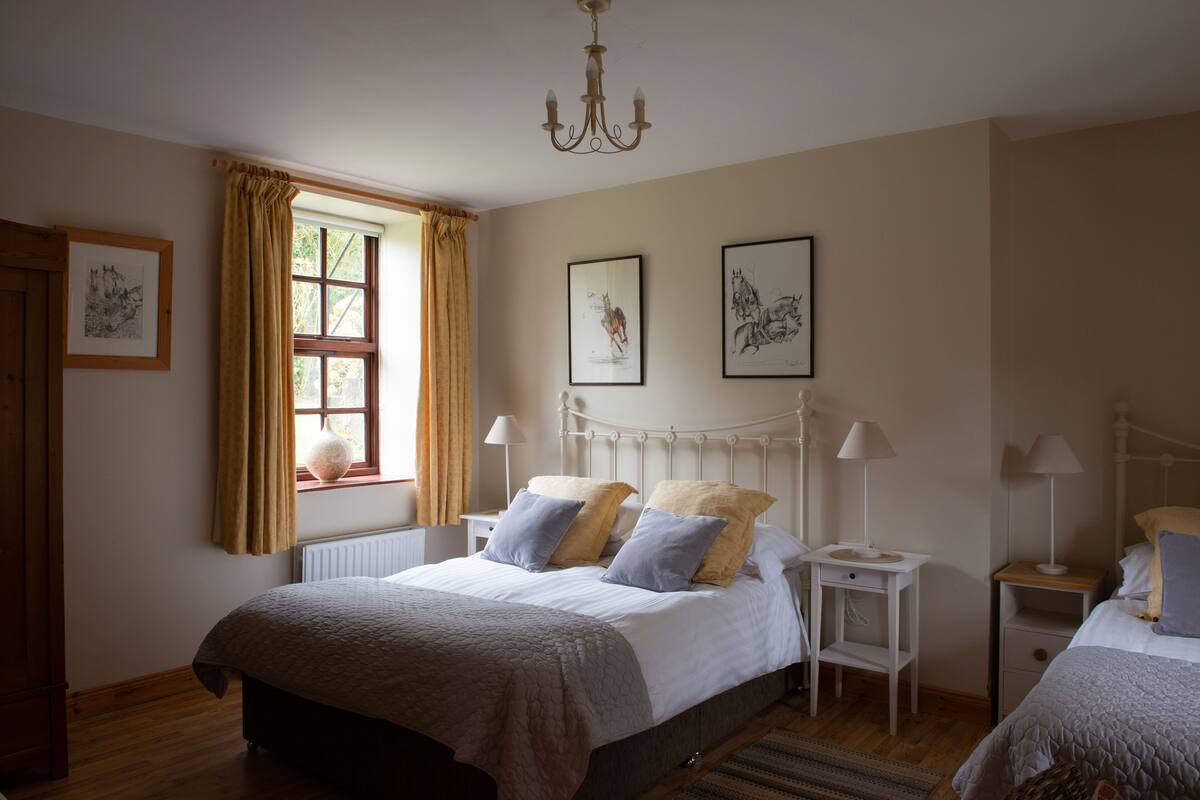 A bedroom with a large bed, two bedside tables, a window with curtains, and wall-mounted artwork.