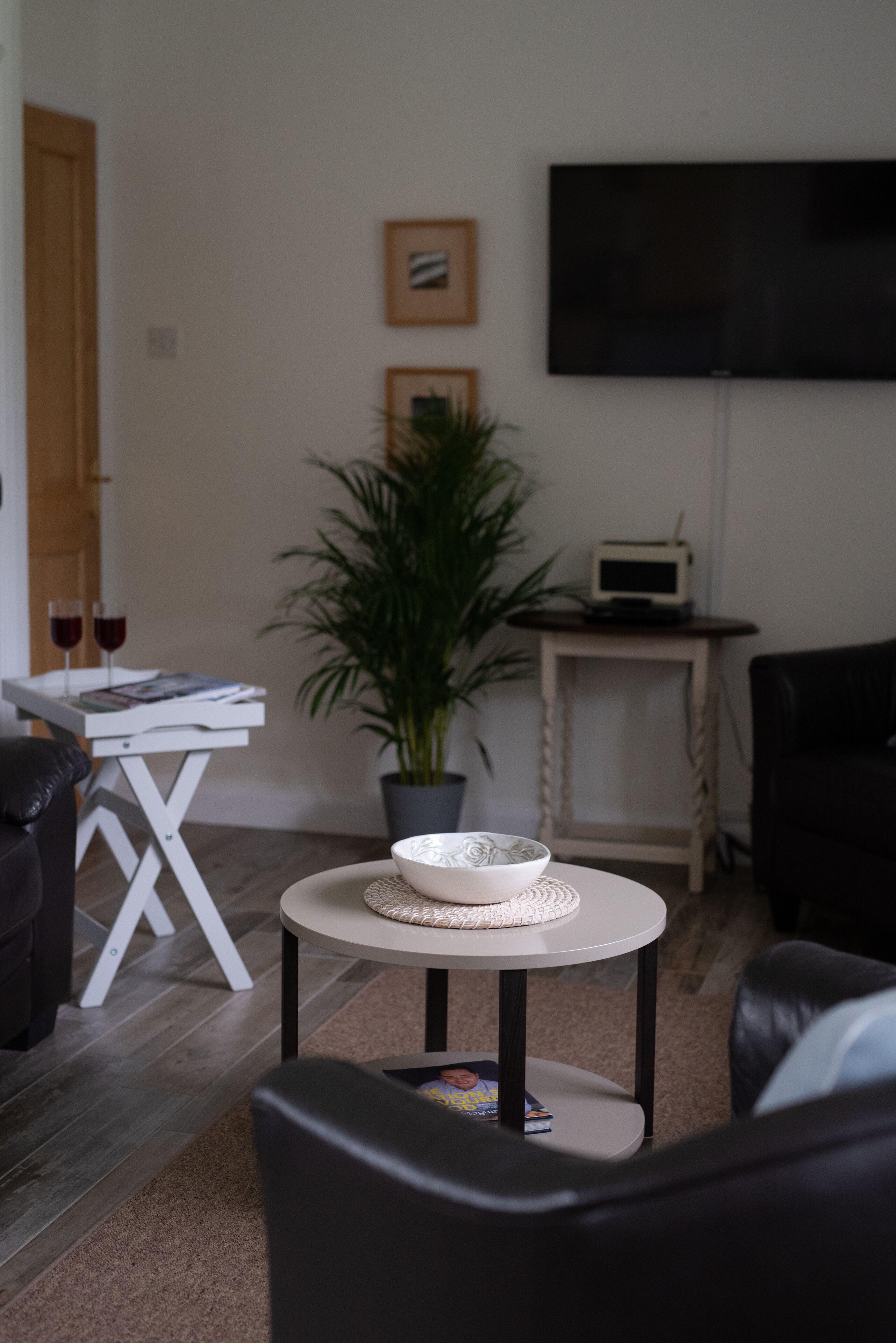 Una sala de estar con un sofá, una mesita con un cuenco, una planta en maceta, un televisor de pantalla plana y una pequeña mesa con un dispositivo.