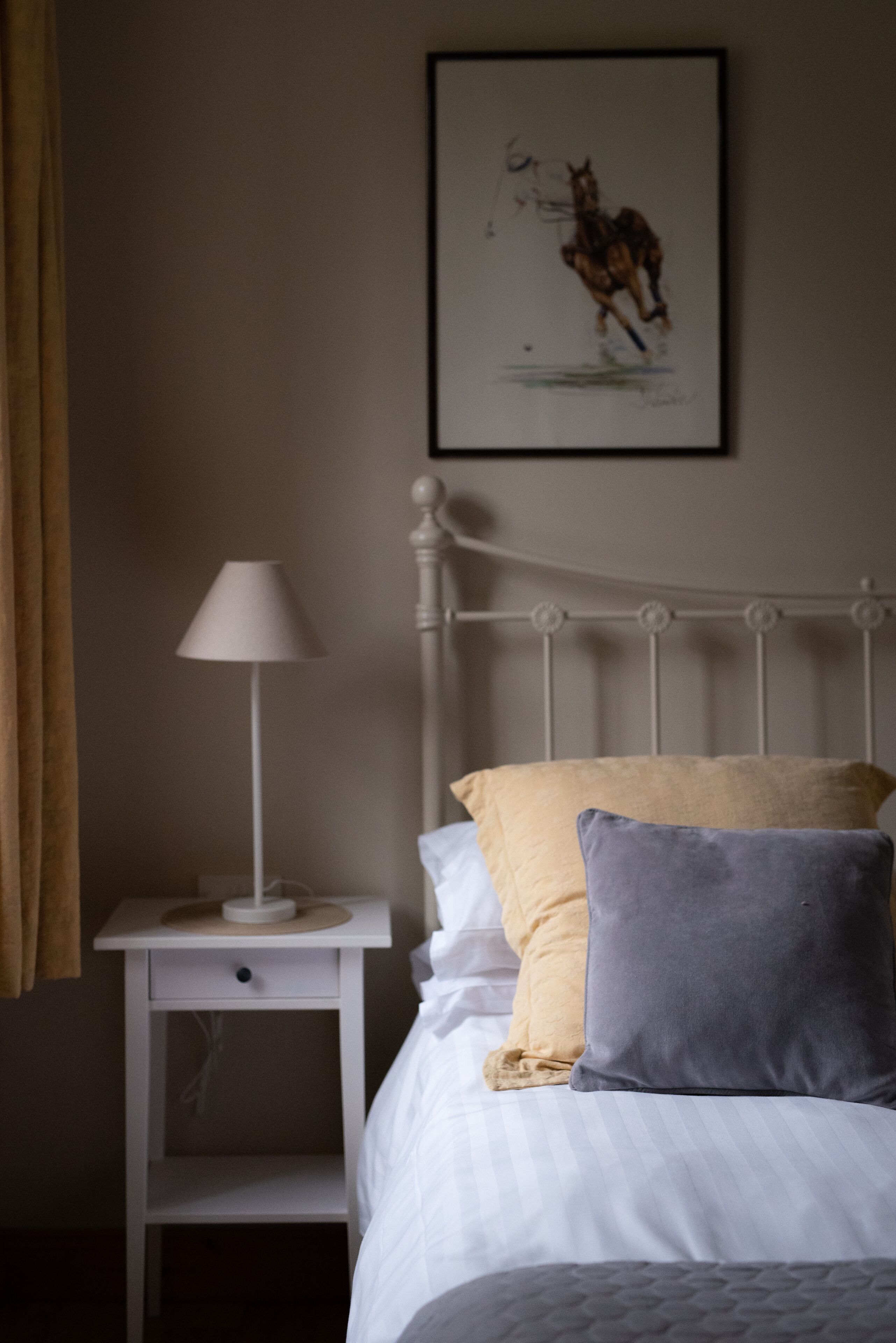 A neatly made bed with white and gray bedding, a bedside table with a lamp, and a framed picture on the wall.