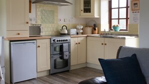 A compact kitchen with a built-in oven, a small refrigerator, and a stove. There is a window with a view of the outside, and a brown leather sofa in the living area.