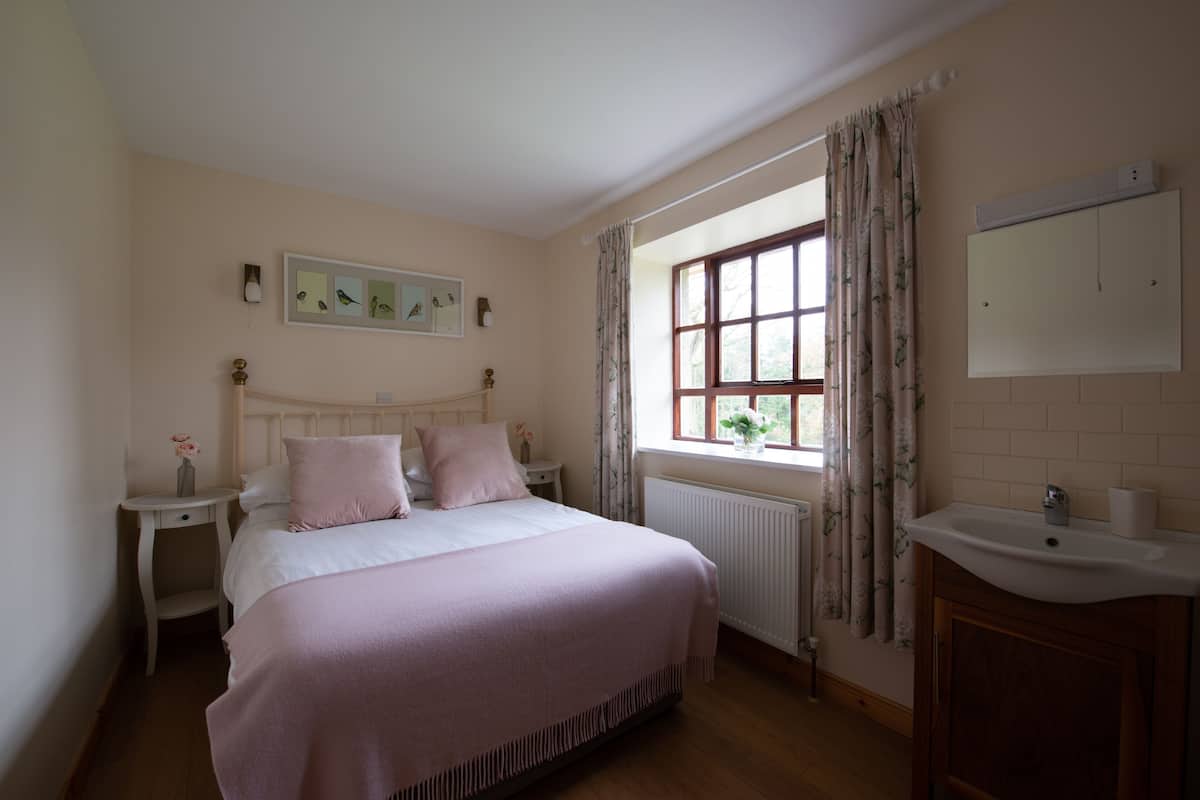 A bedroom with a bed, bedside tables, a window with curtains, a radiator, and a sink.
