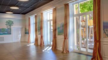 A spacious room with large windows, wooden flooring, and decorative curtains.