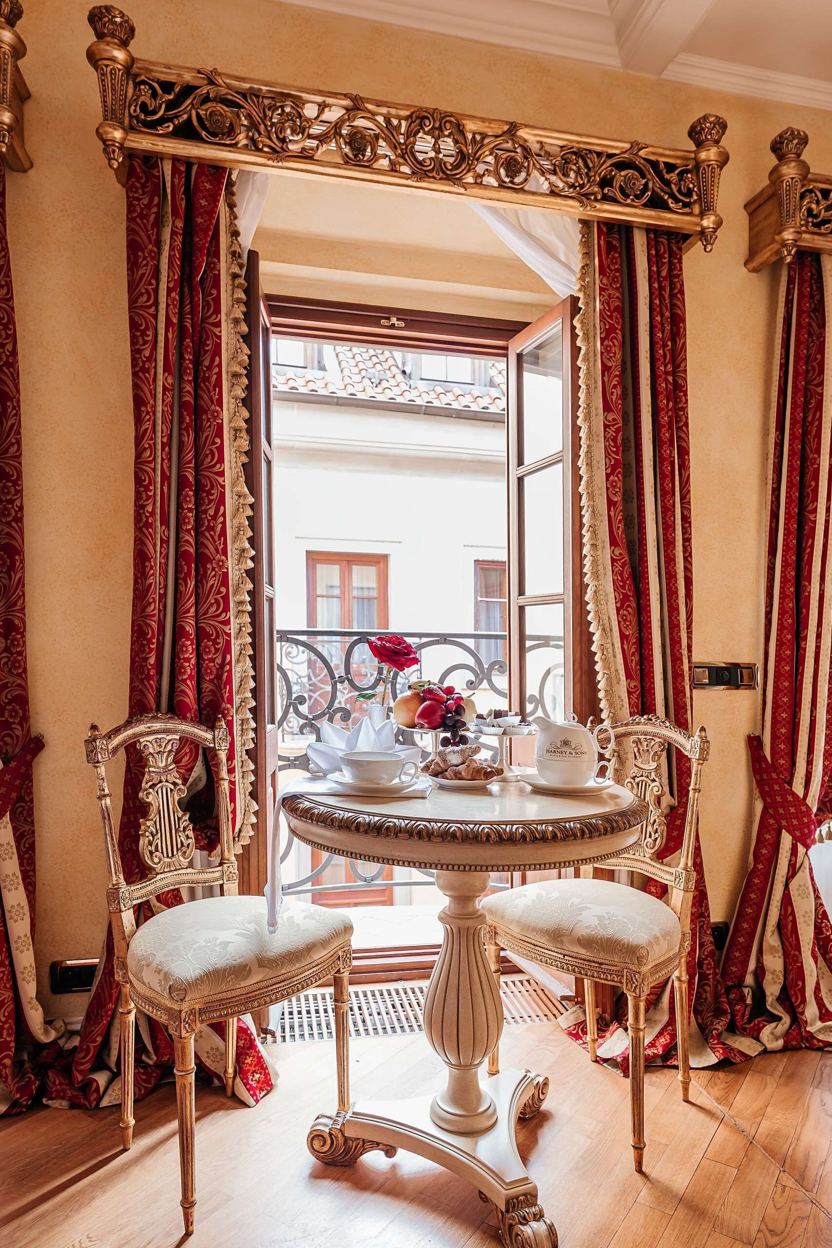 A room with ornate furniture, a balcony with a view, and a table set with a teapot and cups.