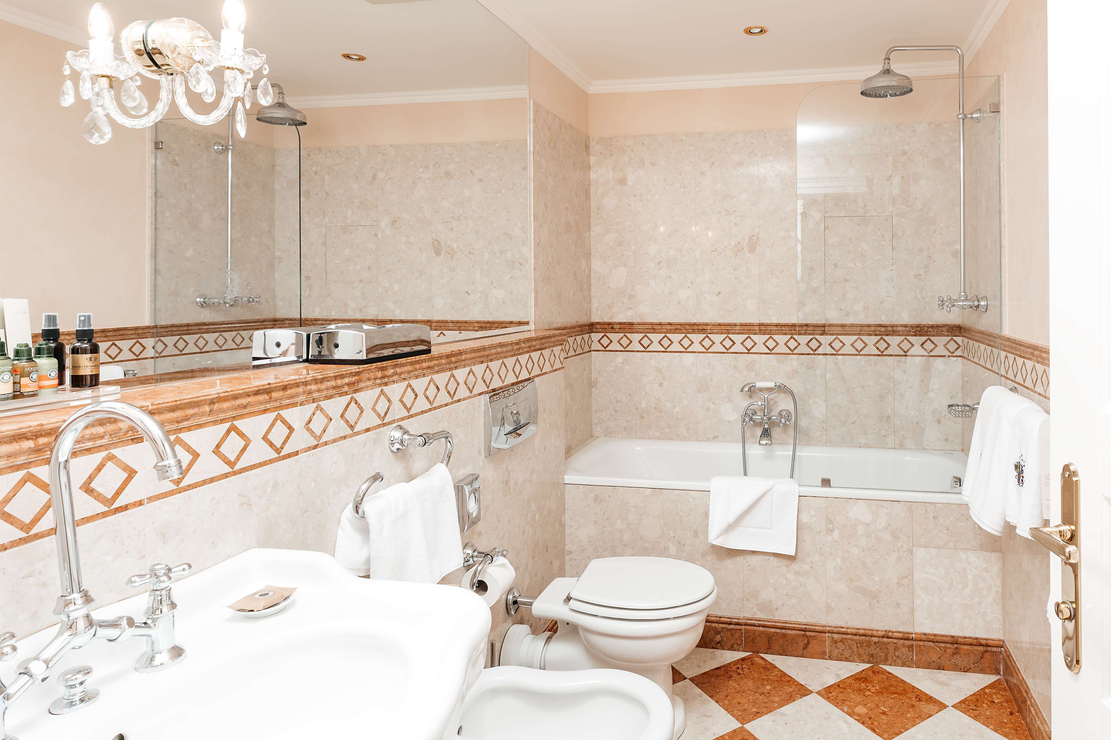 A bathroom with a sink, toilet, and bathtub, featuring a mirror, chandelier, and patterned tiles.