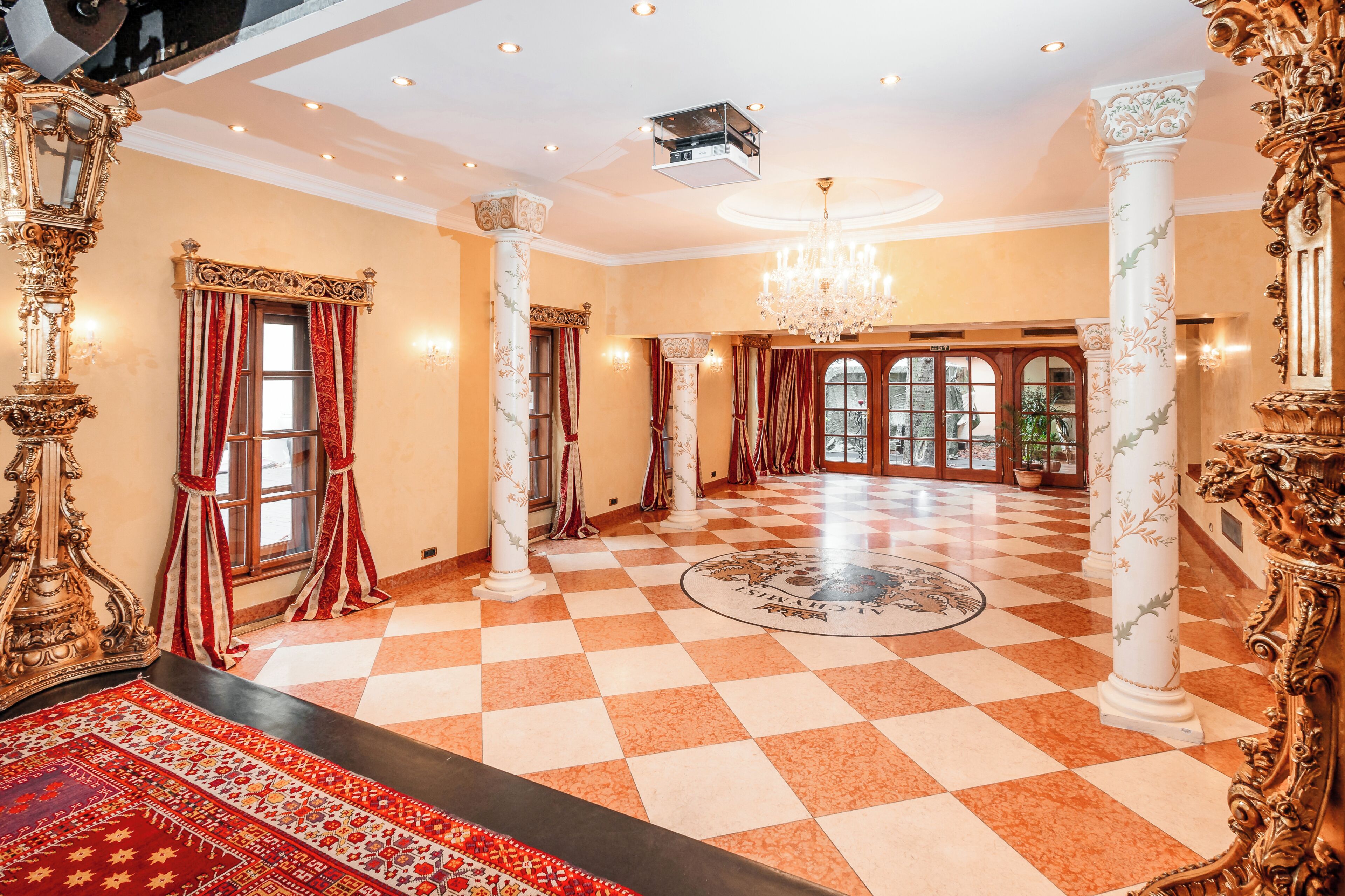 A spacious room with ornate columns, a checkered floor, and a chandelier.