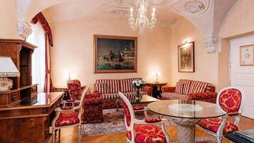 A room with a round glass table, red and white striped sofas, and a chandelier.