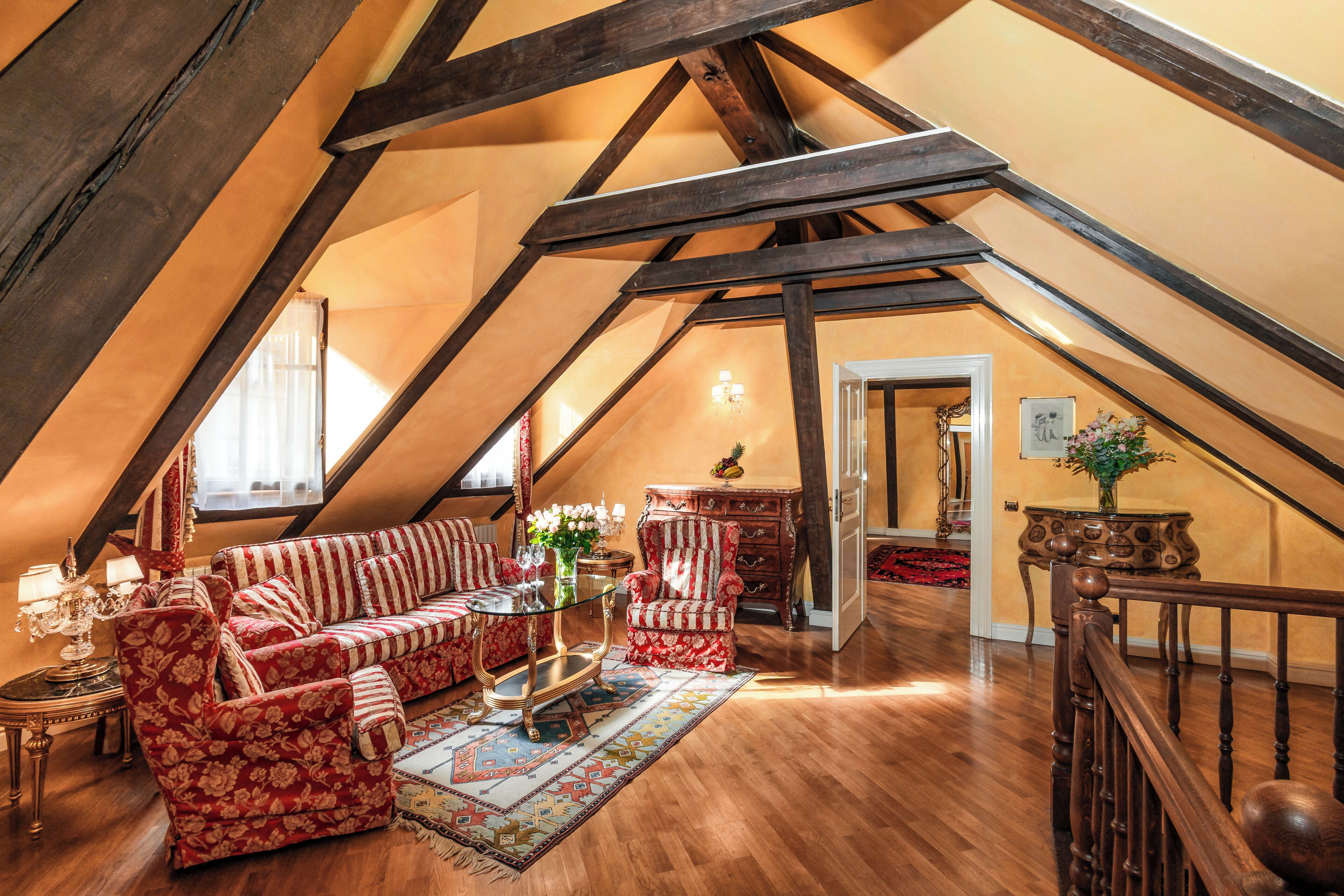 An attic room with a wooden ceiling, a sofa set, a chair, a table, and a staircase.