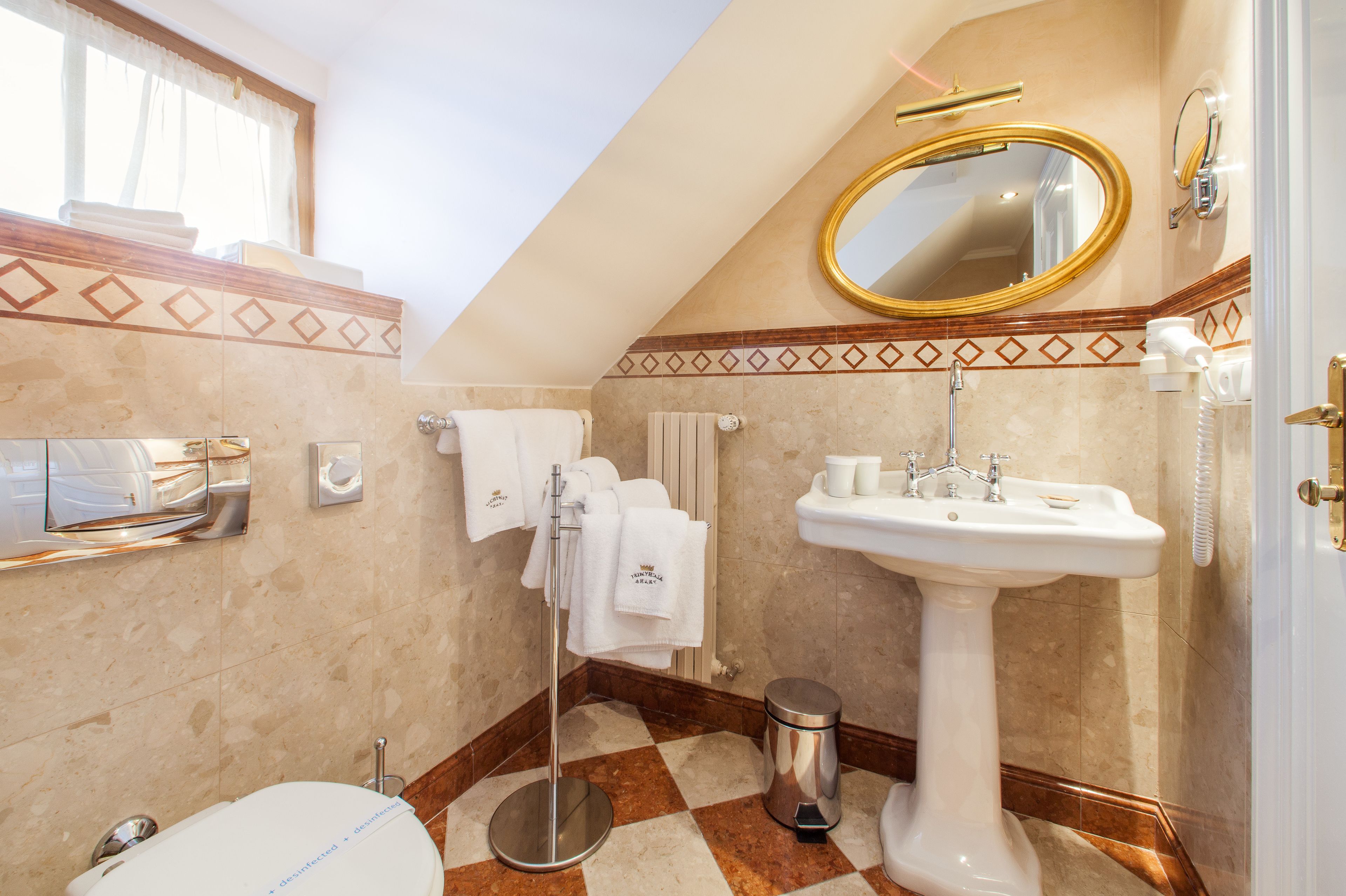 Un baño con lavamanos pedestal, espejo, toallero y retrete.