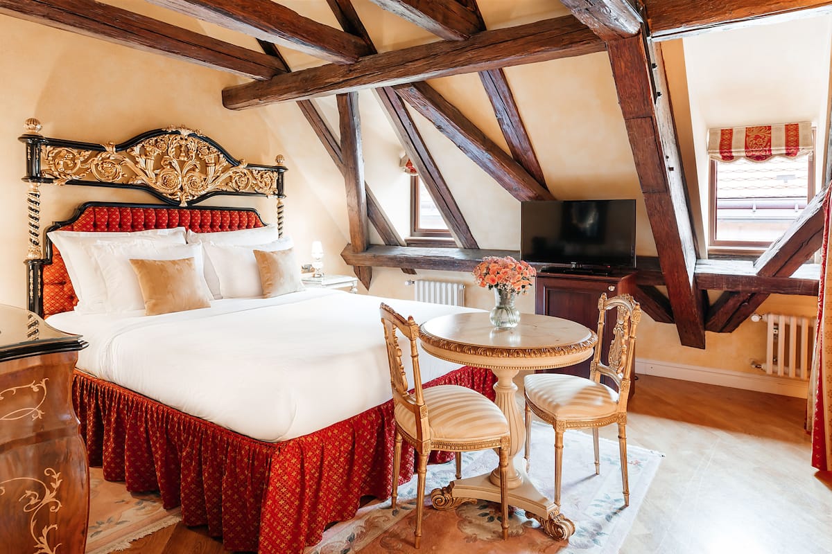 Ein Schlafzimmer mit einem großen Bett, einem Fernseher, einem Esstisch mit Stühlen und einem Fenster mit Vorhängen.