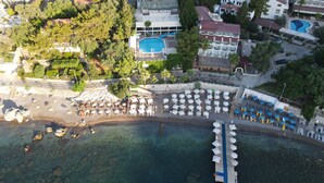 An aerial view of a coastal resort with multiple buildings, a swimming pool, and a beach area with umbrellas and lounge chairs. - Mavi Deniz Otel - All Inclusive (Marmaris)
