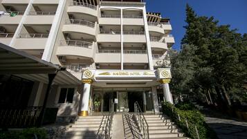 A multi-story hotel with a central entrance, balconies on each floor, and a clear sky.