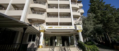 A multi-story hotel with a central entrance, balconies on each floor, and a clear sky.