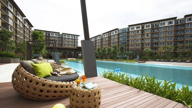 A poolside area with a wooden deck, a lounge chair, and a small table with a drink. - Bann Thew Lom By Paninthira (Cha-am)