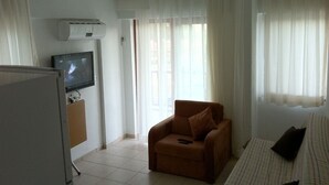 A living room with a television, a sofa, a chair, and a large window with curtains. - Gaye Apart (Ula)