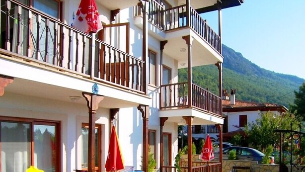A two-story building with balconies, a garden with flowers, and a mountain in the background. - Gaye Apart (Ula)