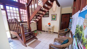 A wooden staircase leading to a second floor, a dining area with wicker chairs, a table with a vase of flowers, and a wall with framed artwork. - Pousada Brisa de Paraty (Paraty)