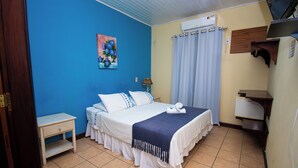 A bedroom with a bed, a nightstand, a painting, an air conditioning unit, and a window with curtains. - Pousada Brisa de Paraty (Paraty)
