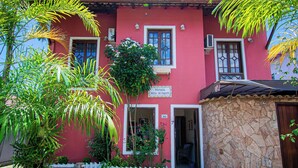 A red building with a stone wall entrance, a white picket fence, and a clear blue sky. - Pousada Brisa de Paraty (Paraty)