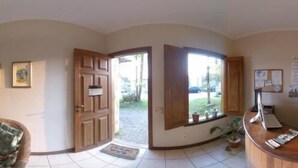 Uma área de recepção com uma mesa de madeira, um banco acolchoado e uma porta que dá para o exterior.