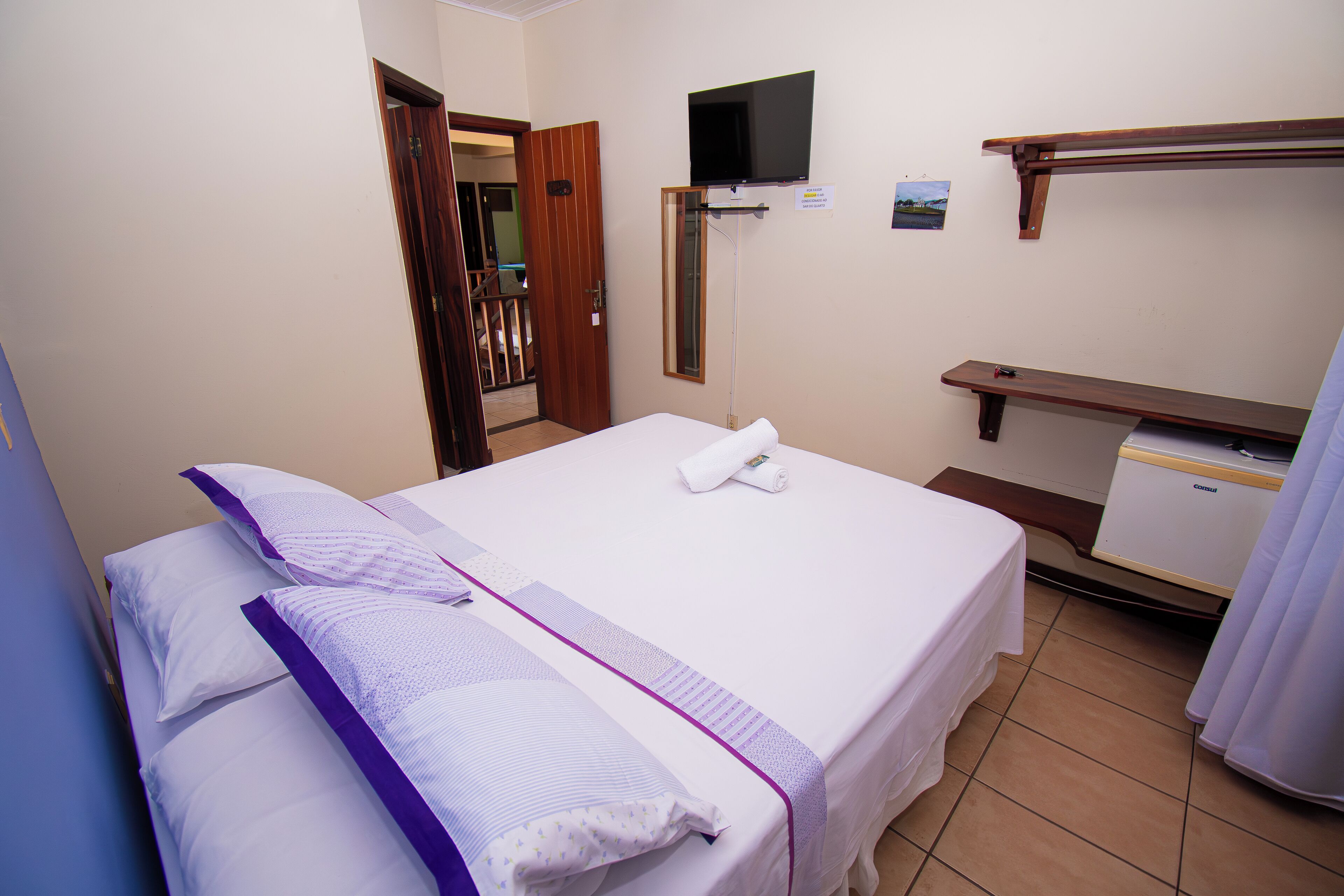 Una camera d'albergo con un letto, una televisione a parete, una scrivania e una sedia.