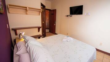 A bedroom with a bed, a nightstand, a desk, a television, and a door leading to another room.