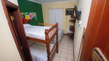 Una habitación pequeña y estrecha con una cama de madera, una pared verde, una cortina blanca y un televisor pequeño en la pared.