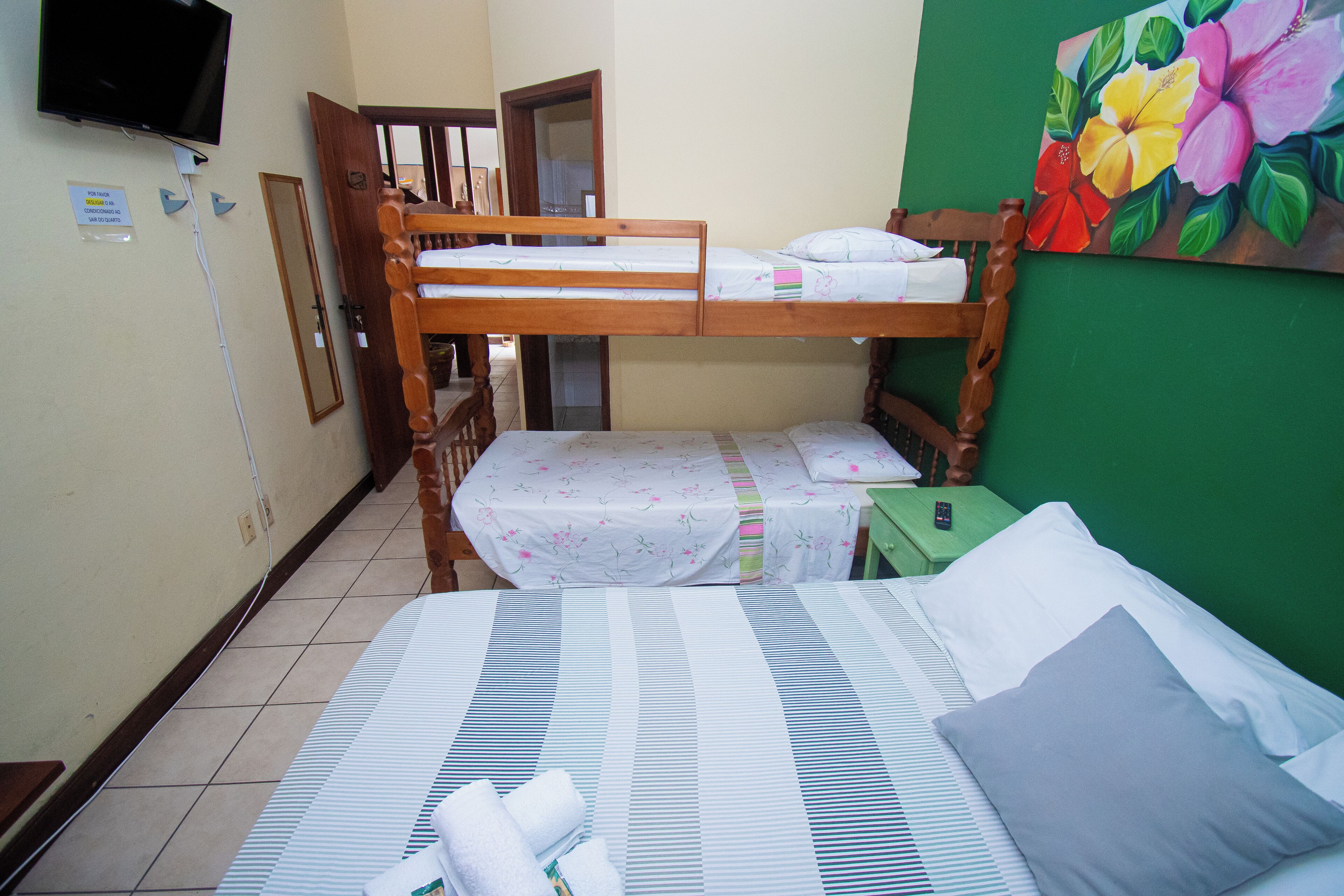 Habitación con literas, un televisor en la pared, un cuadro de flores y una pared verde.