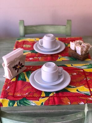 A small table with two white cups and saucers, a basket of books, and a floral tablecloth. - Pousada Brisa de Paraty (Paraty)