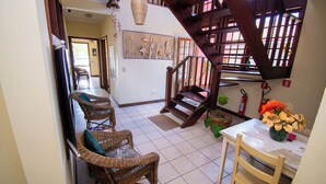 A dining area with wicker chairs, a wooden table, and a staircase leading to an upper level. - Pousada Brisa de Paraty (Paraty)