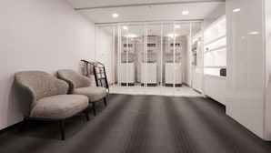 A modern office space with two upholstered chairs, a whiteboard, and a glass partition with a view of a kitchen area. - The Carlton (Taichung)