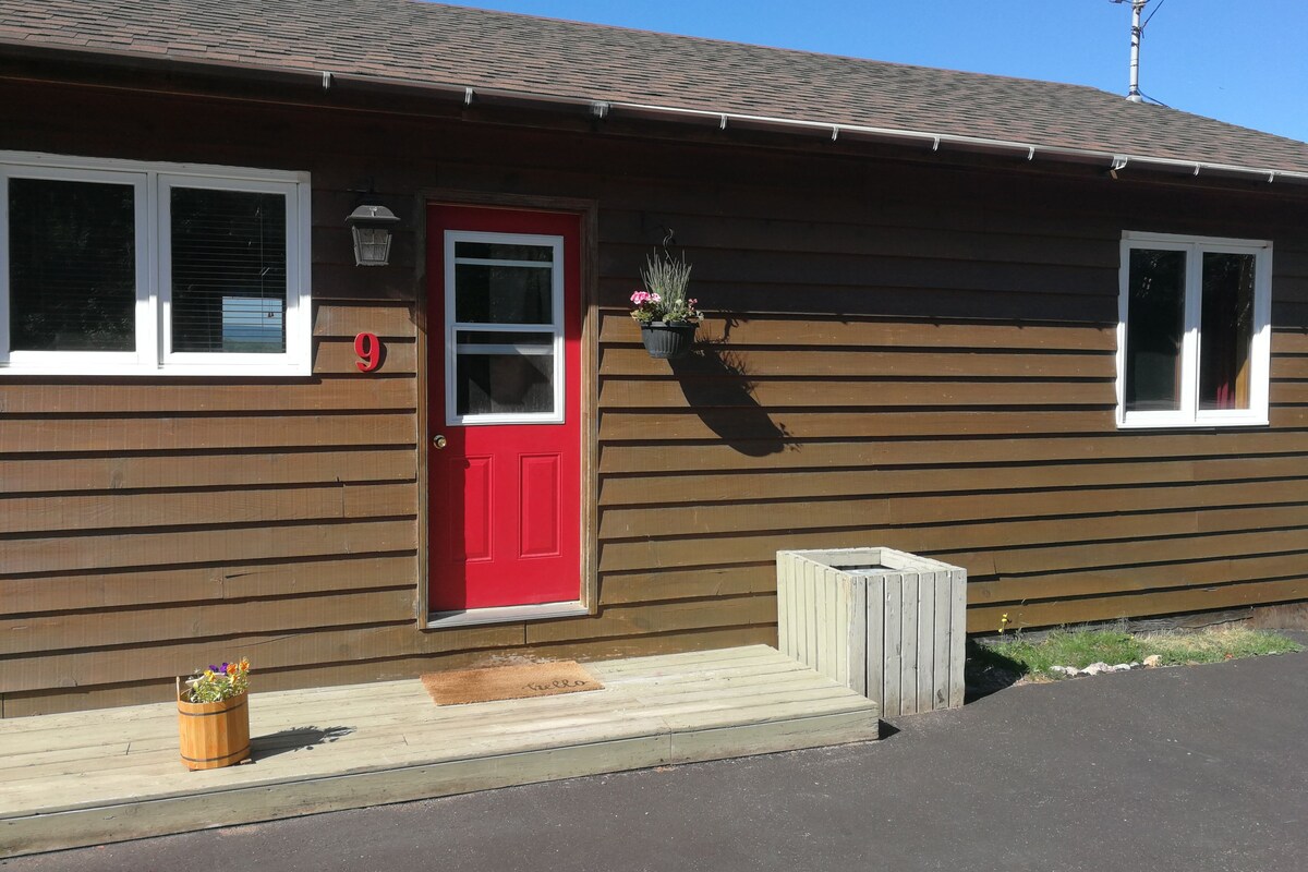 A wooden house with a red door, a mailbox, and a small porch area.