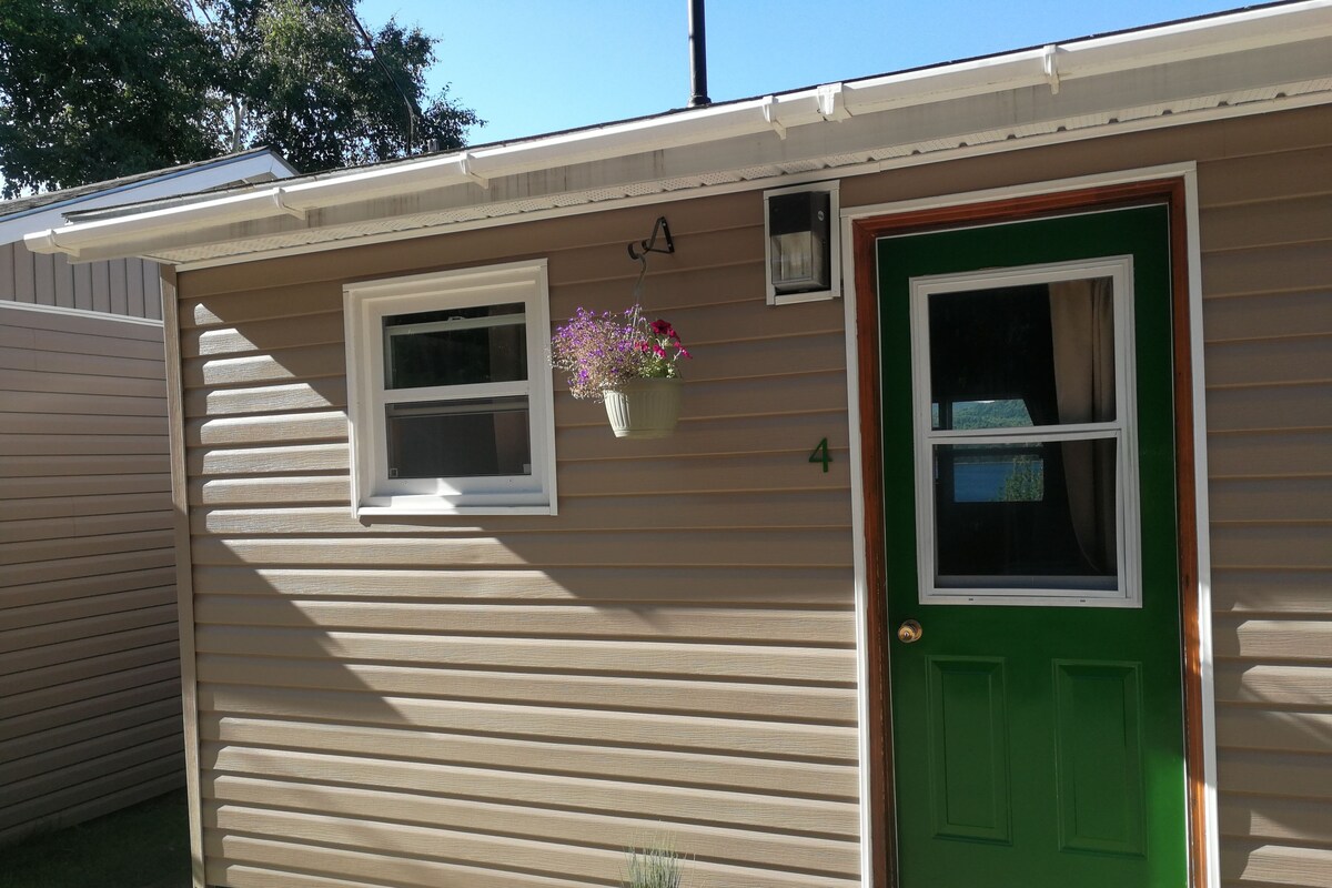A single-story building with a green door, a small window with a hanging flower pot, and a number '4' on the wall.
