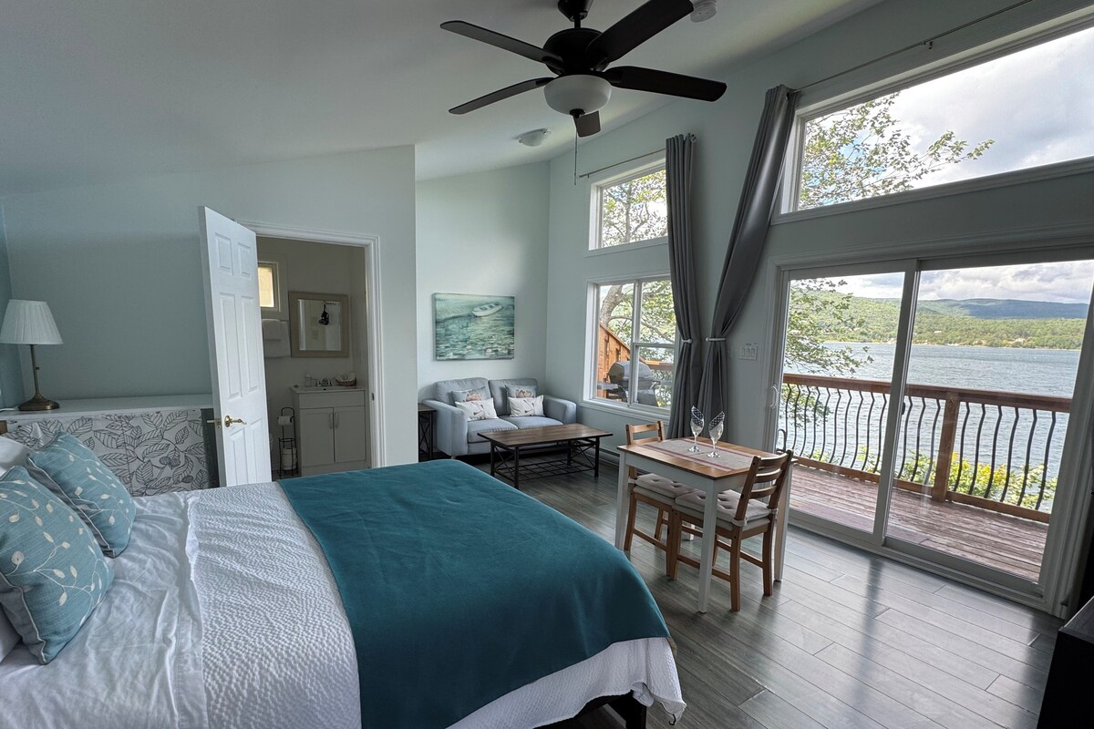 A bedroom with a bed, a desk, and a view of a lake.