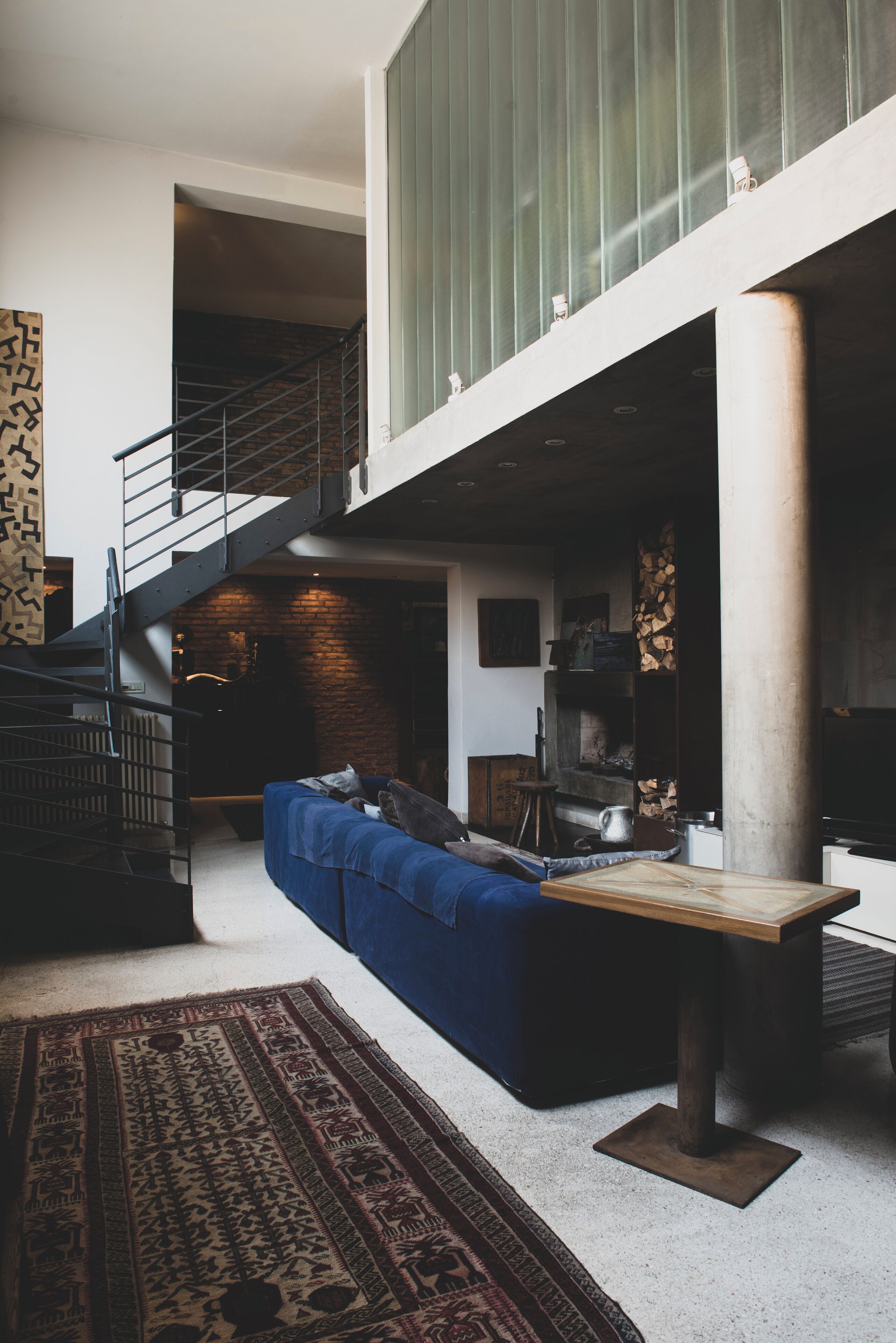 Ein modernes Wohnzimmer mit einem blauen Sofa, einem Holztisch und einer Treppe, die zu einer oberen Ebene führt.