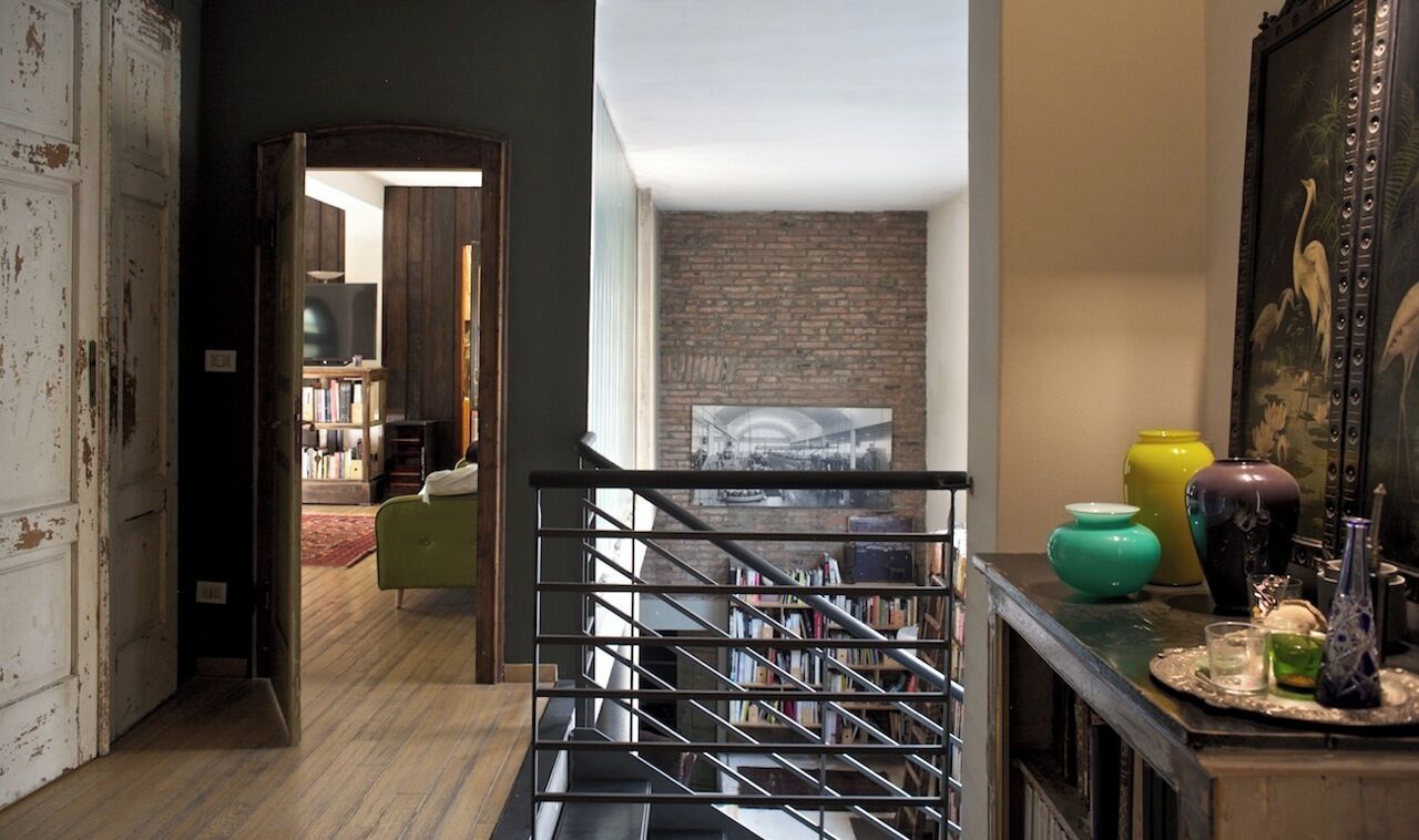 A staircase with a metal railing leading to a lower level. There is a bookshelf with various books and a framed picture on the wall.