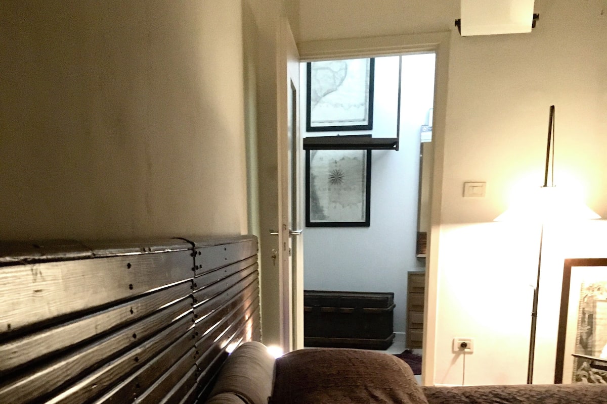 Quarto com cabeceira de madeira, cama com manta marrom, mesa de cabeceira e abajur.