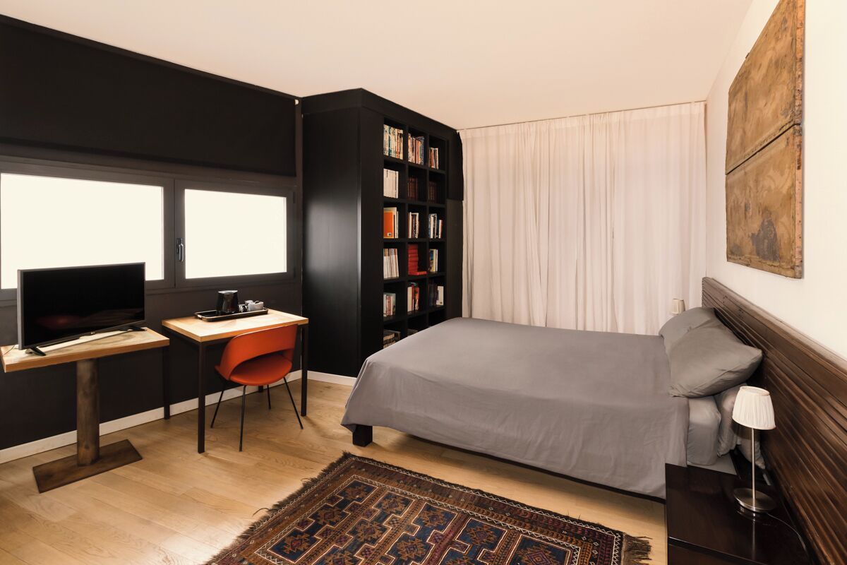 A modern bedroom with a bed, a desk with a TV, a bookshelf, and a window.