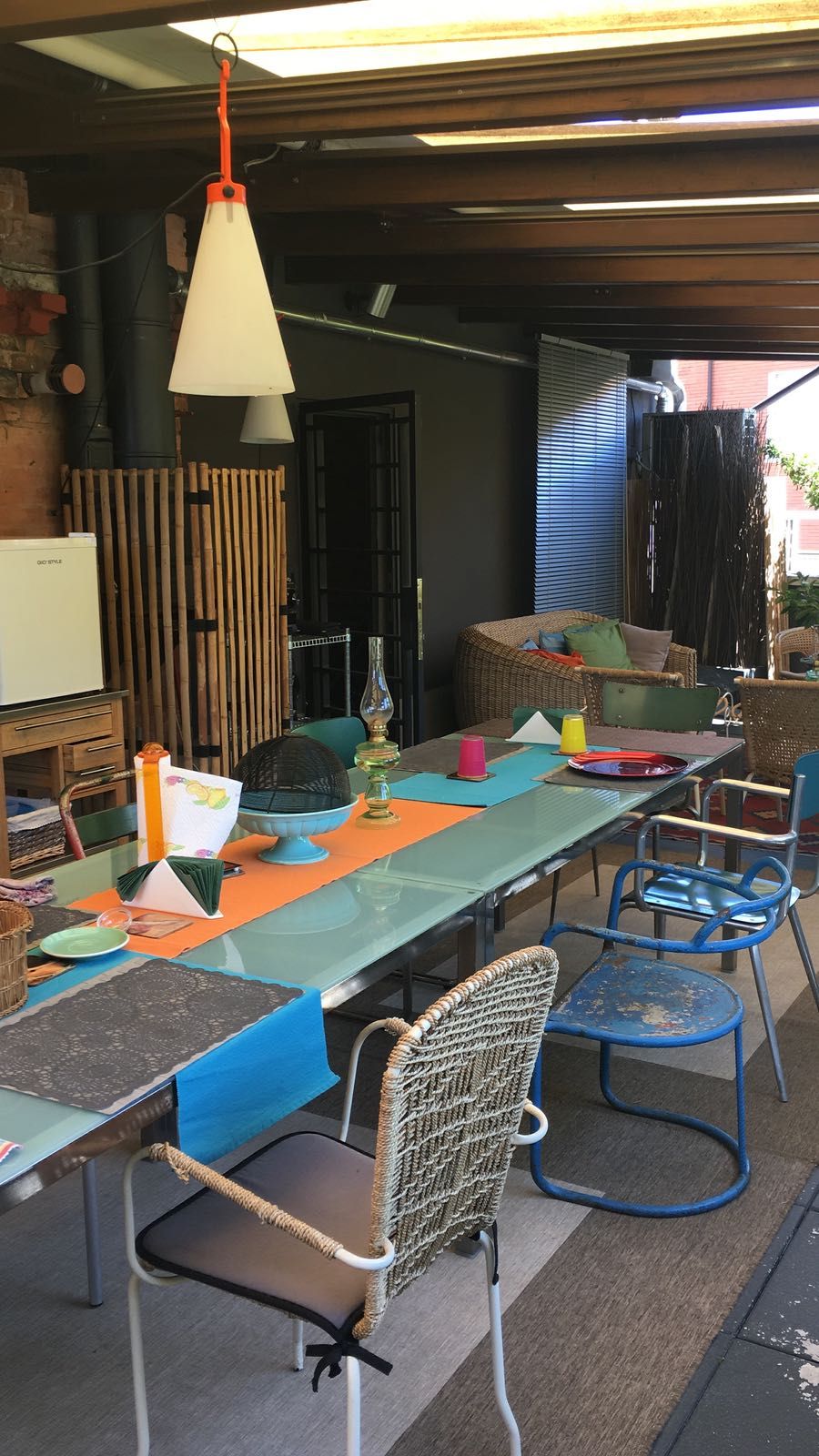 An outdoor dining area with a long table, chairs, and a hanging light fixture.
