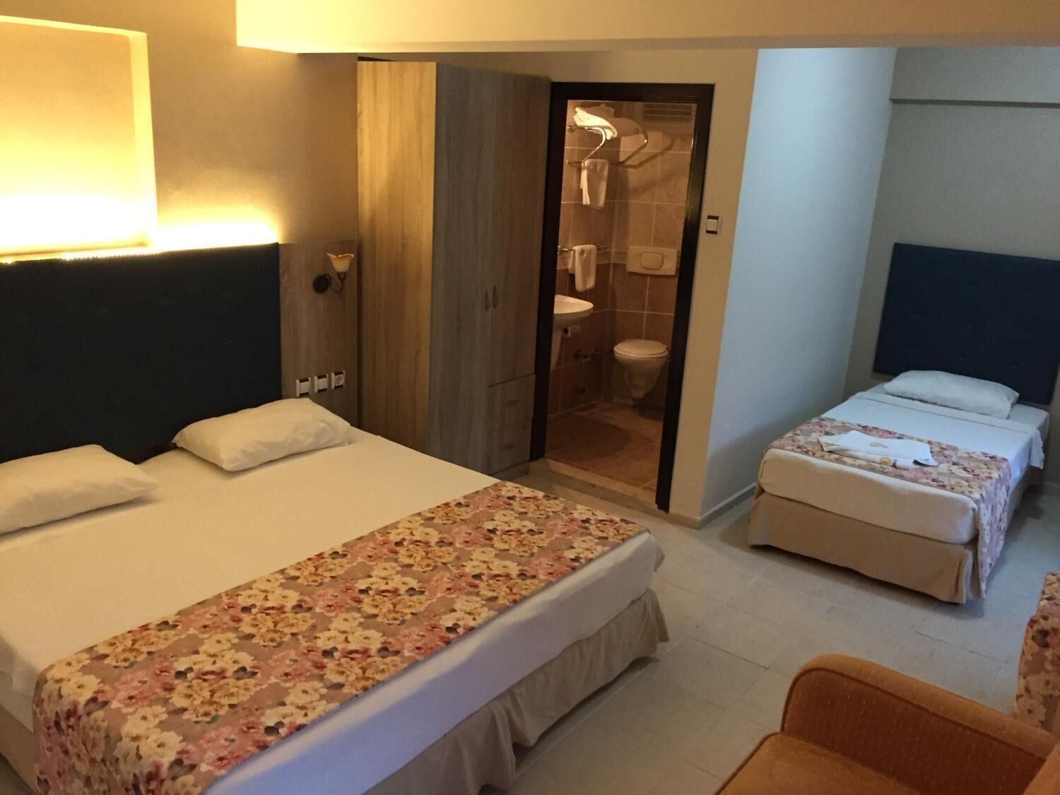 Une chambre d’hôtel avec deux lits, une armoire, une salle de bain et un petit coin salon.