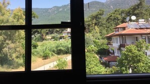 A view through a window of a building with solar panels on the roof, surrounded by greenery and mountains. - Hamle Hotel (Ula)