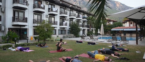 A group of people exercising outdoors on a grassy area with a building in the background.