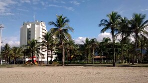 Ett hotell vid stranden med en sandstrand, palmer och en h ög byggnad i bakgrunden.