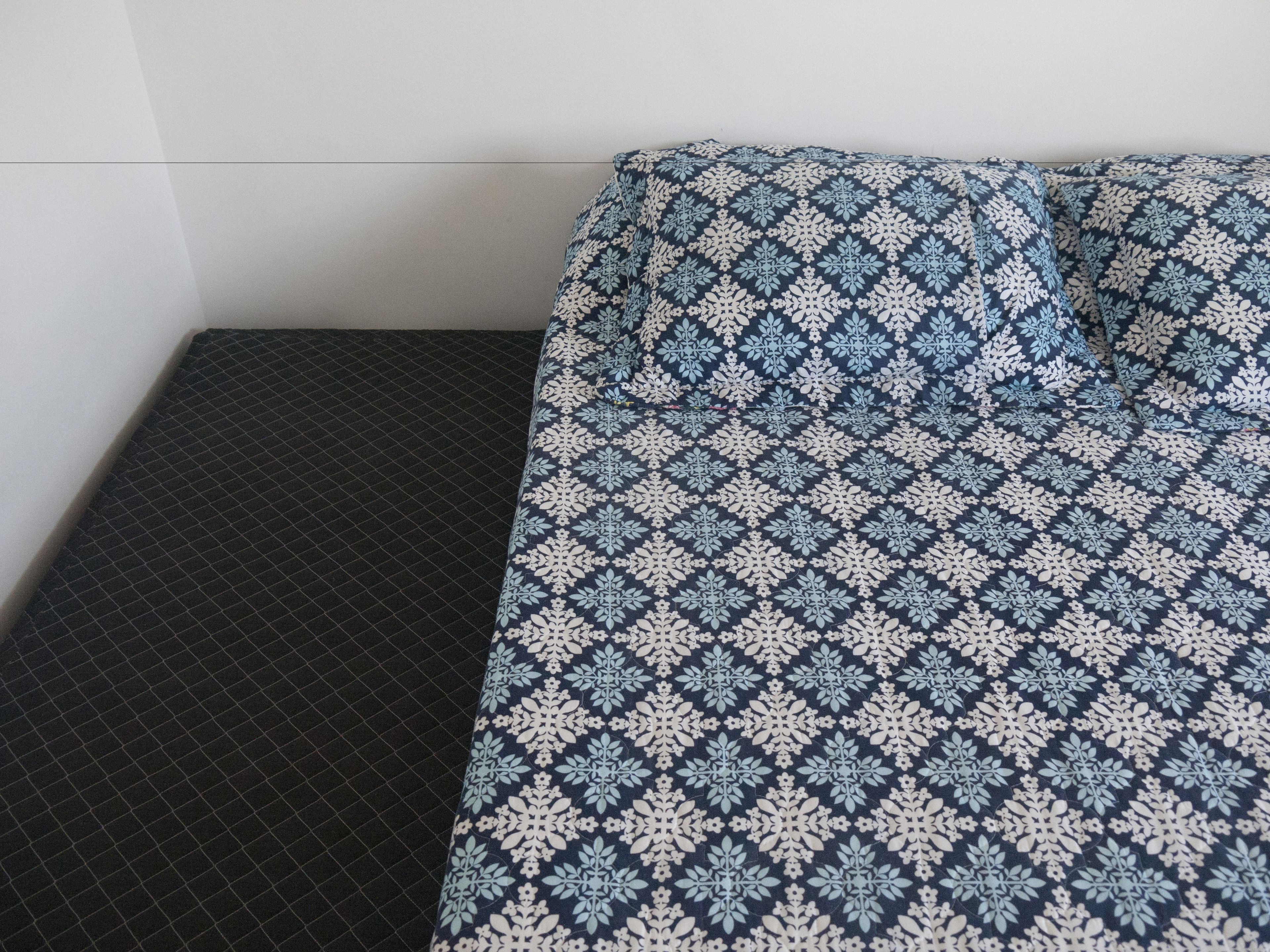 A bed with a patterned bedspread and a dark, textured pillow.