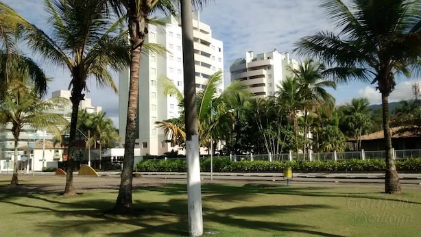 A park with palm trees and a white building with multiple floors. - Doce Lar de Bertioga (Bertioga)