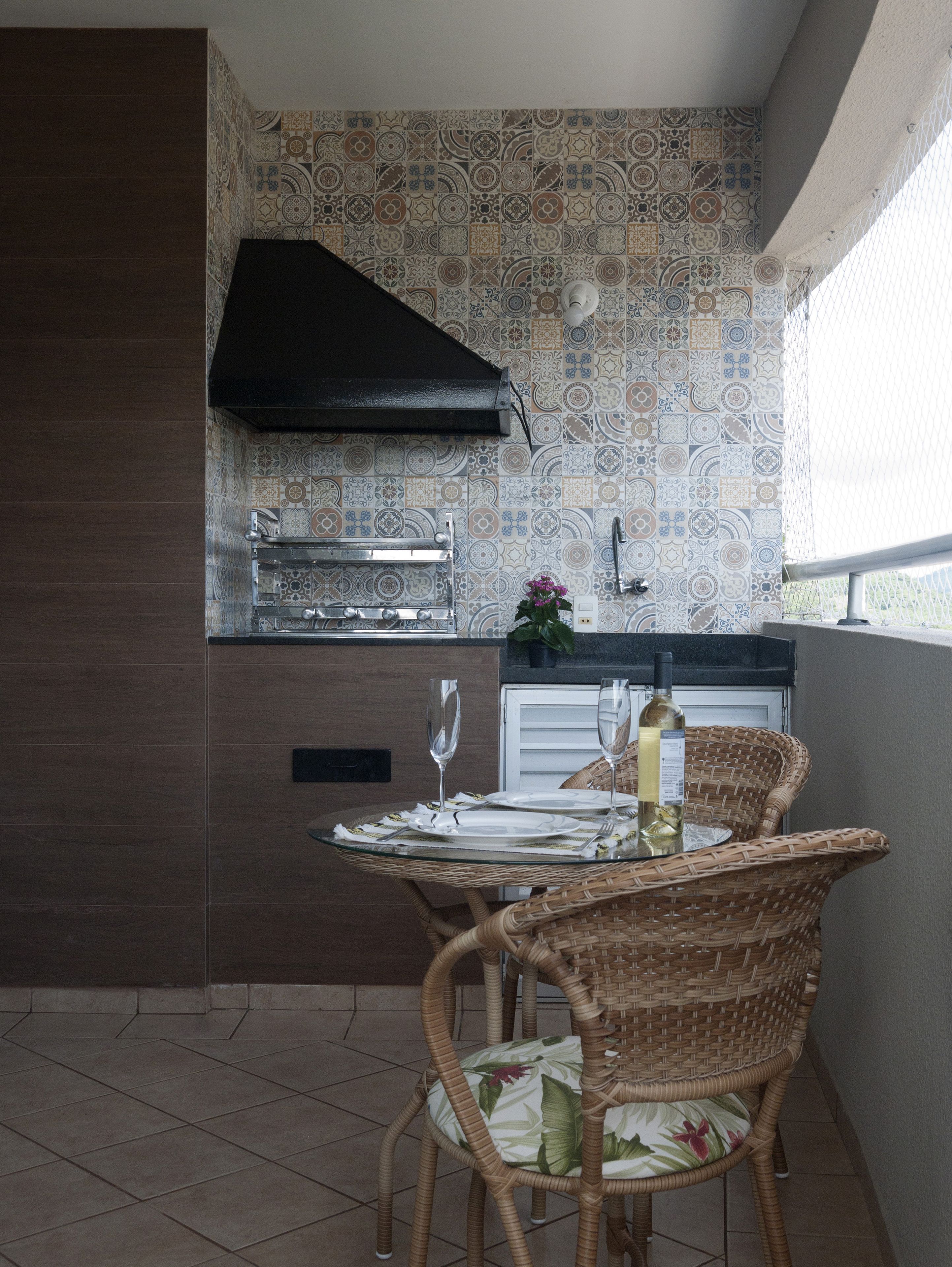 A kitchen with patterned tiles, a black hood, and a dining area with wicker chairs and a table set for two.